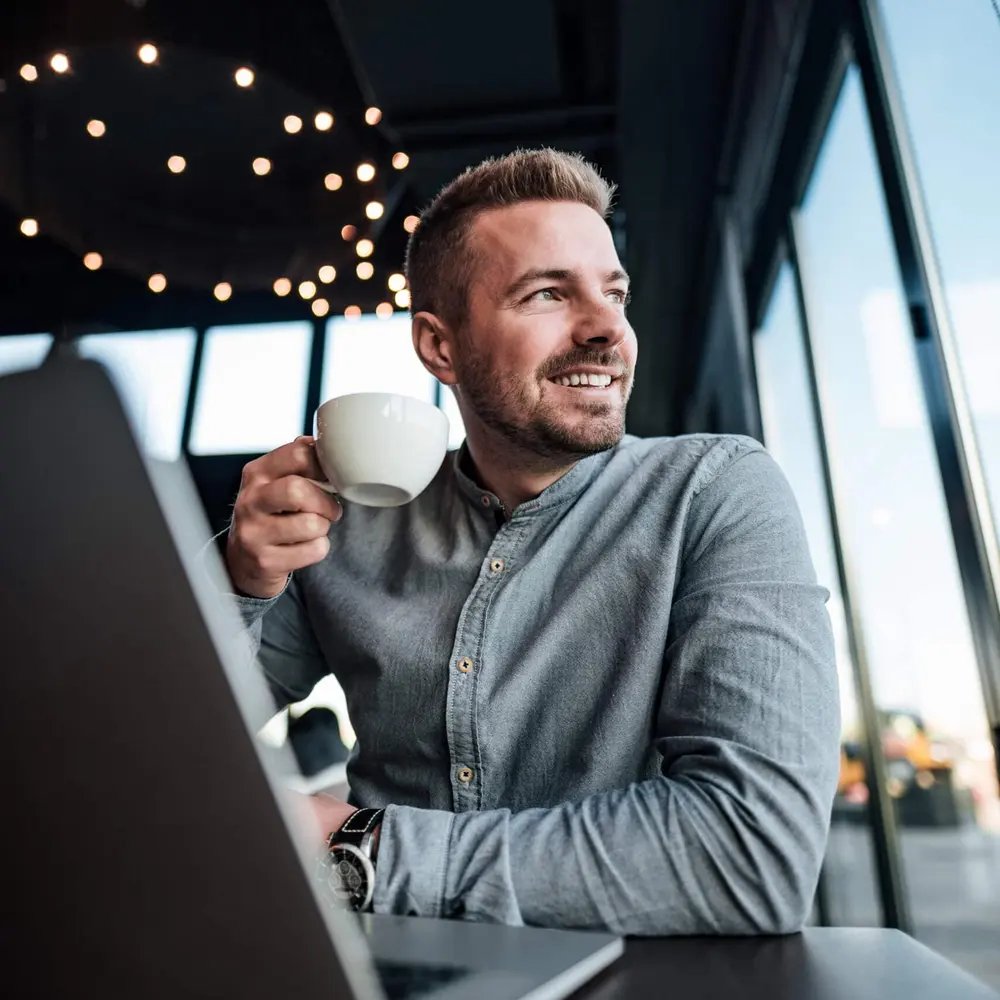 Ondernemer met laptop en koffie kijkt tevreden op